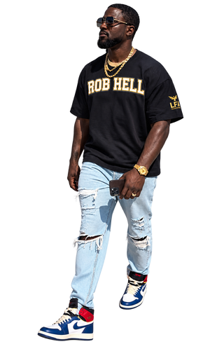 A man wearing a black t-shirt with 'ROB HELL' printed in gold across the chest, light-wash ripped jeans, blue and white sneakers, and gold jewelry, set against a solid white background.